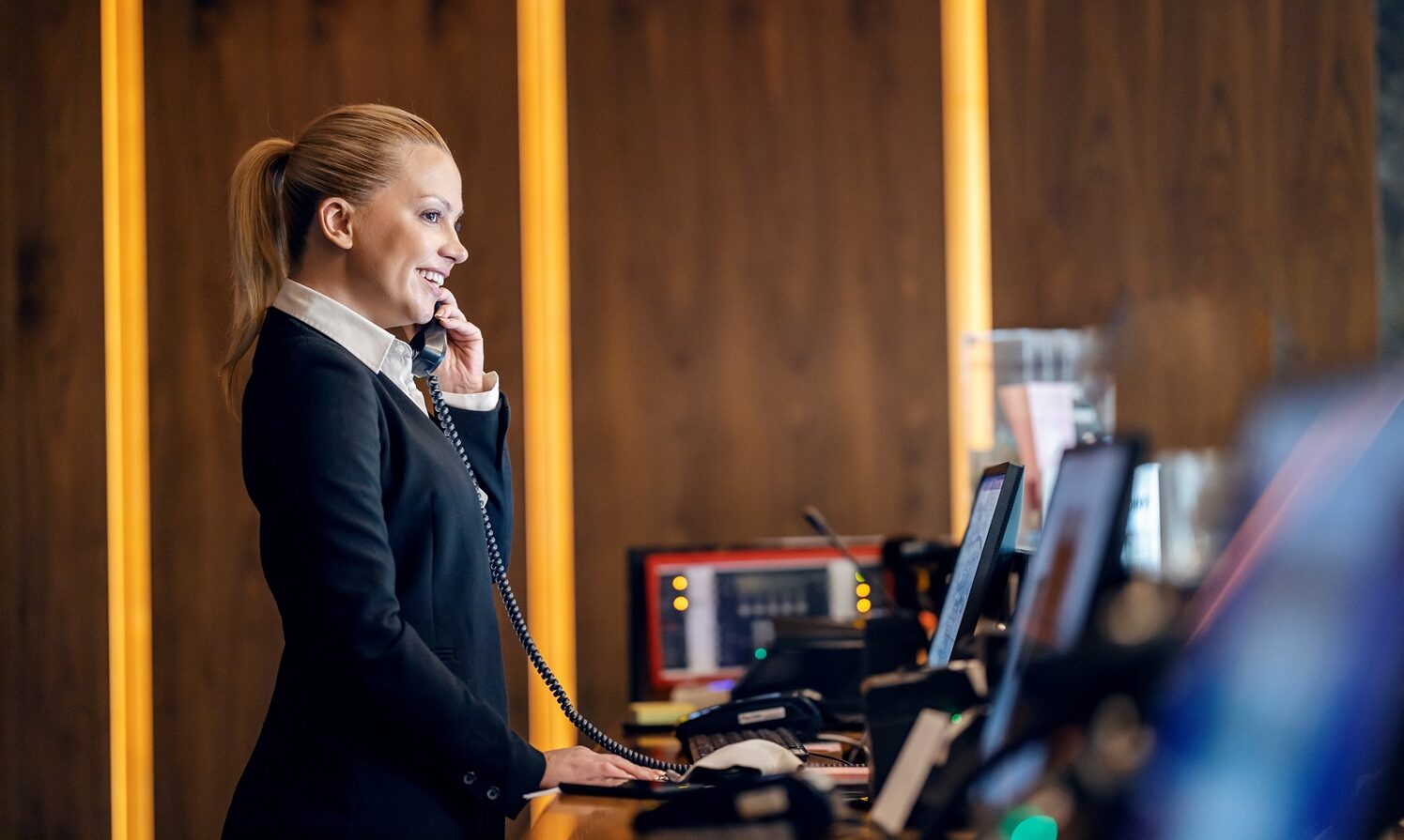 A friendly receptionist at reception is talking on the phone with hotel guest.