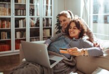 Young lesbian couple online shopping from a laptop on the couch at home